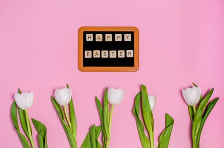 Chalk board with the words Happy Easter and a bouquet of white tulips on a pink background, copy space, flat lay. The concept of the holiday, spring. View from above.の写真素材
