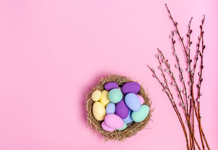 Easter eggs colored in a decorative nest of straw and pussy-willow branches on a pink background, copy space, flat lay. Place for text. The concept of the holiday, spring. View from above.の写真素材