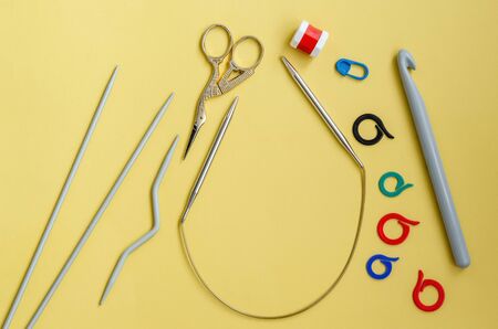 Knitting tools on a yellow background. Pins, markers, row counter, knitting needles and crochet hooks, scissors close-up with copy space, flat lay. Top view, hobby.の写真素材