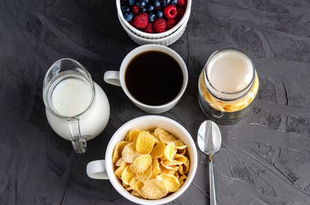 Healthy breakfast with cornflakes in a white cup, berries, milk and coffee on a dark gray background. Copy space for your text, healthy snack, quick breakfast. View from above.の写真素材