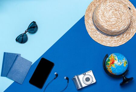 Table top accessory women plan to travel in a festive background concept. Mobile phone, headphones, sunglasses, hat, globe, passports, camera on blue paper with creative design space.の写真素材