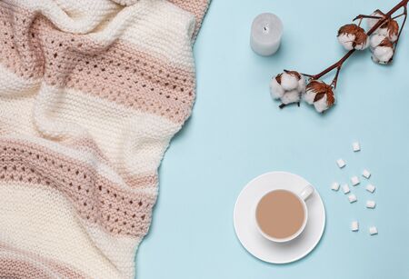 Cup with cappuccino, marshmallows, white candle, cotton flower, croissant, light pastel giant plaid, bedroom, morning concept, on blue background. View from above. Flat lay, copy space.の写真素材