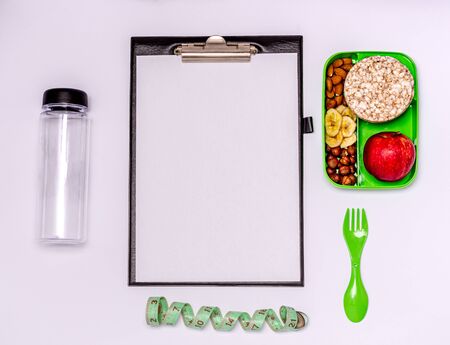 Healthy snack, healthy lifestyle, menu planning. Apple, nuts, banana chips, bread rolls in a food container.Water bottle, tape measure, tablet with paper for notes.Flat lay, copy space.View from aboveの写真素材