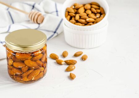 Almond nuts in flower honey in a glass jar on a white background. The concept of a healthy and healthy snack, healthy lifestyle, natural sweetness, dessert. Close-up. Flat lay, copy spaceの写真素材