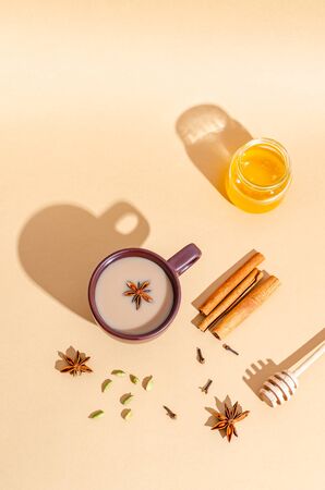Traditional indian tea. Masala tea in a dark clay cup with ingredients, hard shadows. Cinnamon, cardamom, anise, honey, cloves on a beige background. View from above. Copy space for text, flat lay.の写真素材