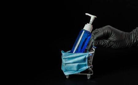 A female hand in a rubber glove rolls a decorative trolley in a protective medical mask, soap in a bank on a black background. Coronovirus, Covid-19, Quarantine, Pandemic.Close-up.Flat lay,copy space.の写真素材