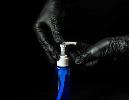 Female hands in rubber black gloves squeeze liquid soap from a blue can for disinfection on a black background. Coronovirus, Covid-19, Quarantine, Pandemic. Close-up. Flat lay, copy space.の写真素材