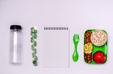 Healthy snack, healthy lifestyle, menu planning. Apple, nuts, banana chips, bread rolls in a food container.Water bottle, tape measure, tablet with paper for notes.Flat lay, copy space.View from aboveの写真素材