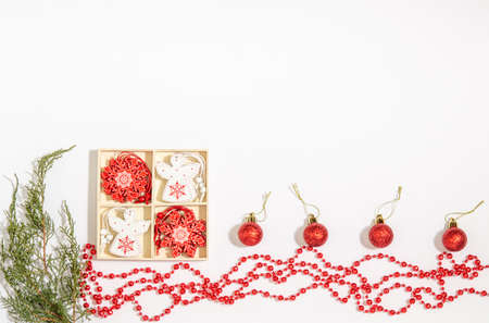Christmas tree toys white angel, red snowflake in a wooden box, red beads, juniper branches, balls on a white background. Space for copy space, flat lay.の写真素材