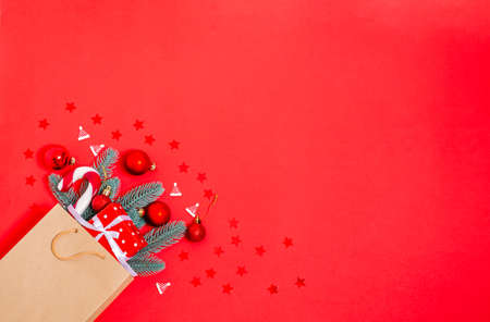 Christmas toys, gift box, fir branches, caramel cane in a paper shopping bag on a red background. Banner, postcard form. Copy space, flat lay. New Year, Christmas, 2021. View from above.の写真素材