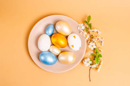 Colored eggs for Easter with branches of blossoming cherry on a blue background. Flat lay, blank for postcard, banner, copy space. Top view,の写真素材