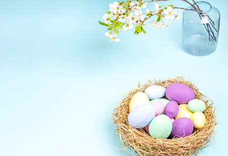 Colored eggs for Easter with branches of blossoming cherry on a blue background. Flat lay, blank for postcard, banner, copy space. Top view,の写真素材