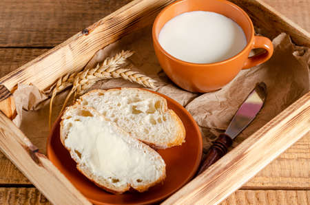 Fresh wheat flour bread with butter and milk in a tray on a wooden background. Breakfast and...