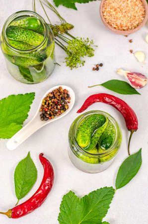 The process of preserving cucumbers with spices and herbs in a glass jar on a white table. Fermentation products, organic and healthy food concept, pickled cucumbers. View from aboveの写真素材