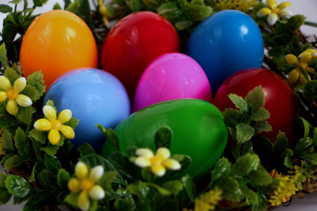 Multicolored decorative Easter eggs in a basket decorated with greens and flowersの写真素材