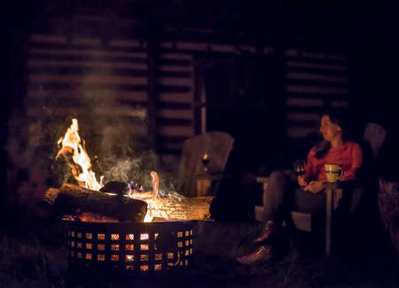 outside fire with a woman enjoying the warmth with a glass of wine with embersの写真素材