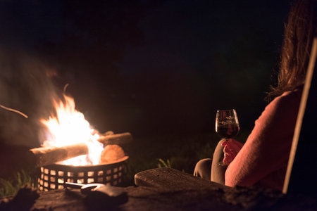 woman intently looks at a fire with a glass of wine at handの写真素材