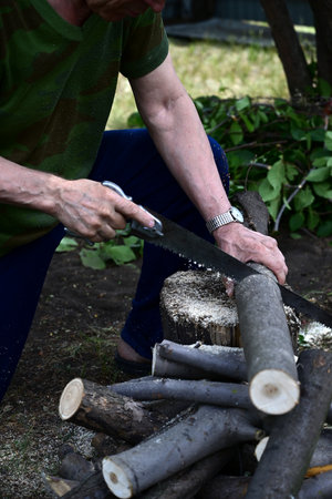 A man with a saw saw off a wooden board. The concept of cleaning in the suburban area.の写真素材