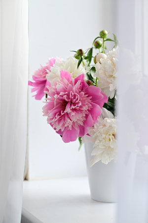 A view of a bouquet of pink and white peonies standing in a vase on the window. Concept background, flowers, holidaysの写真素材