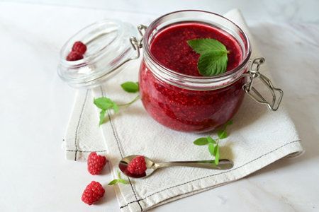 raspberry jam in a glass jar on a white background, tea with raspberries, vitamins for the body