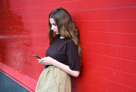 Portrait of a young student reading a message on a mobile phone, a stylish pretty girl chatting on a mobile phone while walking down the streets, social, disorder, disorder, technology, disease, dependentの写真素材