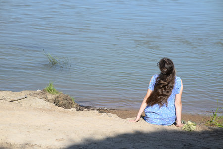 A young girl with long dark hair stands on the bank of the river.の写真素材