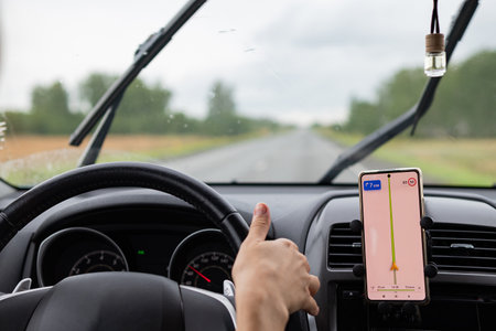 Rear view of a young traveler using a navigator on a mobile phone behind the wheel of a modern car.