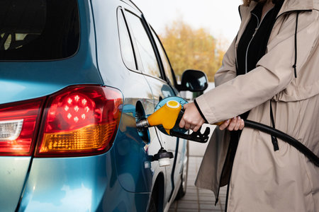 Attractive young woman refueling car at gas station. Female filling diesel at gasoline fuel in car...