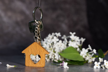 Close-up of the keys and keychain in the form of a house against a background of lilac, a symbol of...