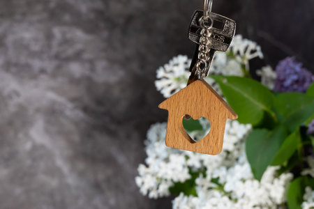 Close-up of the keys and keychain in the form of a house against a background of lilac, a symbol of the family hearth and own home. Purchase of real estate.の写真素材