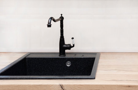A farmhouse kitchen sink detail shot with a black faucet, mosaic tile backsplash, marble countertops, and white cabinets.の写真素材