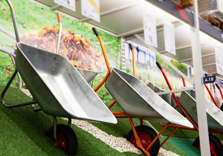 A young man with hands in gloves is carrying a metal garden cart through his beautiful green blooming garden. A professional gardener is carrying a wheelbarrowの写真素材