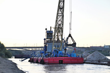 River port. Port cranes on the river bank. Extraction and transportation of sand and other goods. The embankment of the river port, a barge at the mooring wall.の写真素材