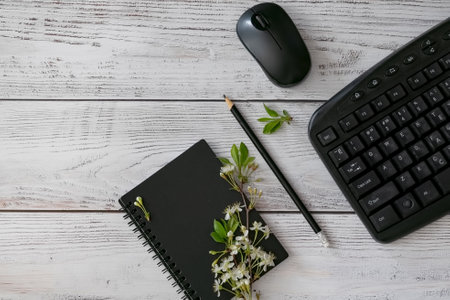 A cozy workspace features a black notebook with a pencil, delicate flowers, alongside a computer...