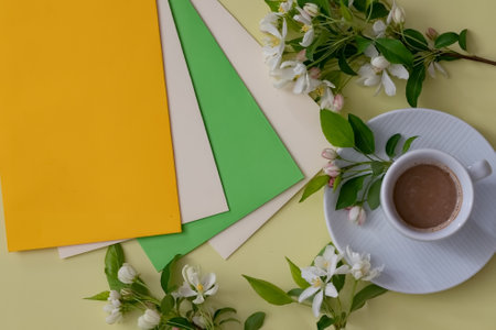 A well-arranged setting features sheets of yellow, green, and beige paper along with a white cup of...