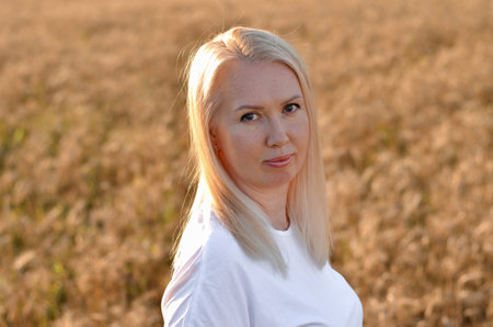 Blonde woman poses confidently in a sunlit wheat field, creating a harmonious connection with nature while enjoying a tranquil evening atmosphere.の写真素材