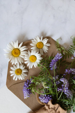Florist at work: a woman prepares a summer bouquet of white gypsophila on a gray desk. Kraft paper, scissors, greeting envelope on the table. View from above. The composition is flat.の写真素材