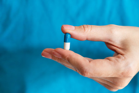 A person is holding a blue and white capsule in their hand in a bright indoor space.の写真素材