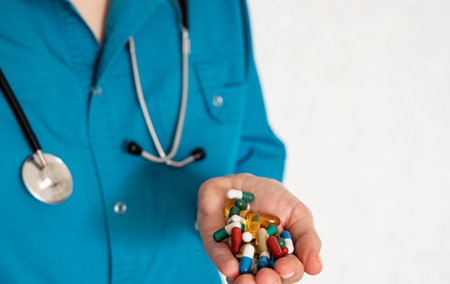 A healthcare worker in a teal shirt displays a collection of colorful pills and capsules in their hand. The setting emphasizes a focus on medication and health.の写真素材