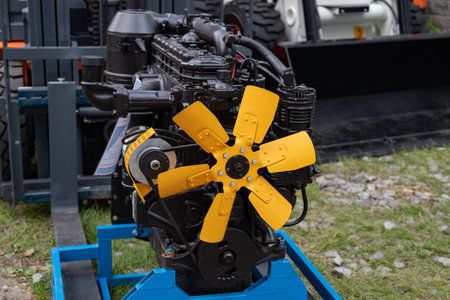 Industrial engine with vibrant yellow fan blades on a blue stand, placed outdoors on grassy ground,...