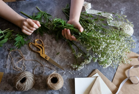 Florist at work: a pretty woman prepares a summer bouquet of white gypsophila on a gray desk. Kraft...