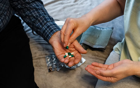 A caregiver transfers medication to a senior citizen in a comfortable living room setting. The interaction highlights the importance of assistance and care at home for the elderly.の写真素材