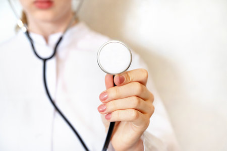 A medical professional in white attire prepares to conduct an examination while holding a stethoscope. The environment suggests a clinical or healthcare setting, emphasizing focus on patient care.の写真素材