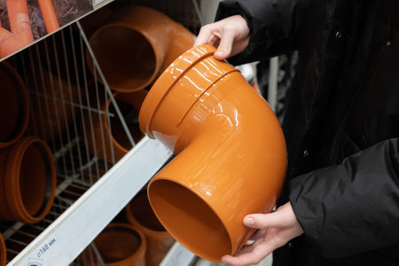 Individual is inspecting a yellow PVC pipe fitting while selecting materials in a home improvement store. Shelves are stocked with various plumbing supplies.の写真素材