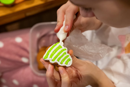 A person decorates a gingerbread cookie with vibrant green icing while seated comfortably in a warm...