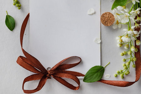 A blank card is elegantly tied with a brown ribbon and surrounded by fresh flowers. The soft white...