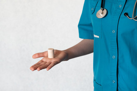A medical professional in a turquoise scrub top holds a small stack of medication on their open palm. The background is neutral, suggesting a clinical environment during daylight.の写真素材