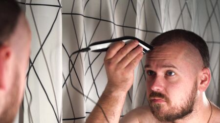 handsome man in the bathroom shaves his head himself with an electric razor.の写真素材