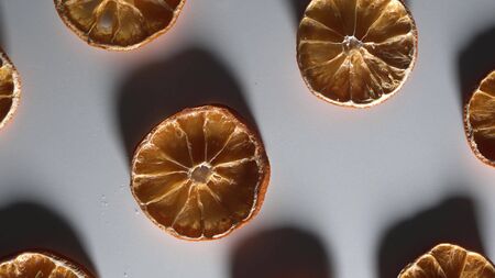Low key light with long shadows. Dry slices orange on white table top down view rotate.の写真素材