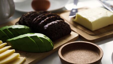 Perfect breakfst. Morning breakfast with cheese, avocado, butter, brown bread, egg. Girl's hand puts white cup or mug with smudges black aromatic coffee on the tableの写真素材